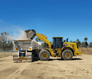 Construction equipment unloading material on a worksite under bright blue sky Yellow wheel loader unloading material into a truck on a construction site under clear skies